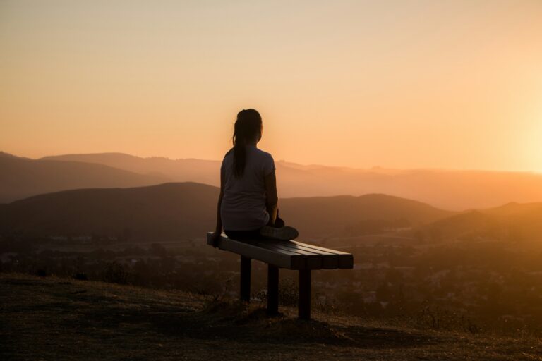 Woman sitting alone on a wooden bench facing mountains — visual metaphor for UPSC Mains essay topic The Process of Self-Discovery Has Now Been Technologically Outsourced.