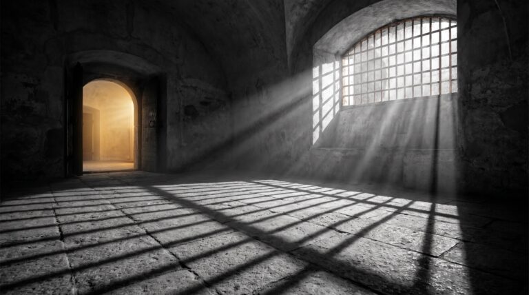Daylight falling between iron bars onto a stone floor with an open doorway beyond