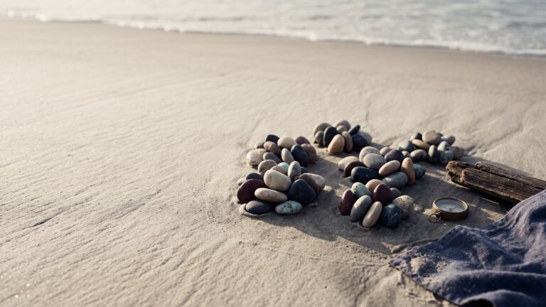 Smooth river stones on wet sand arranged into several distinct tight clusters, tide line beyond.