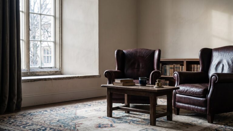 Two heavy leather armchairs facing each other across a low table in a formal room, cold winter light through the window.