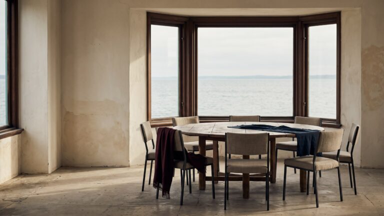 An empty round conference table with eight chairs before a wide bay window looking out over open water.