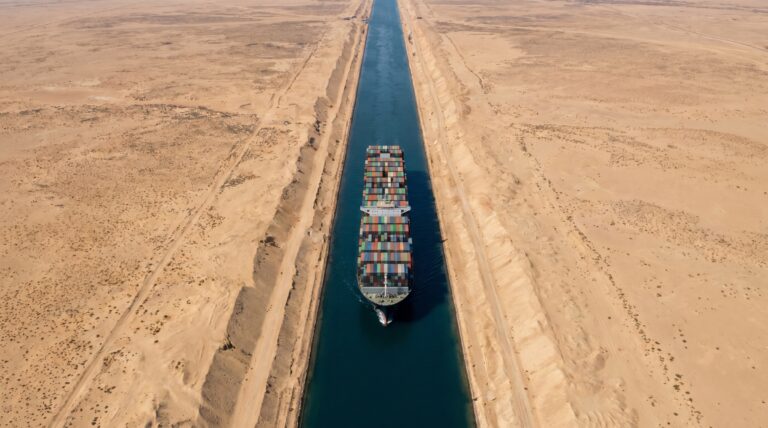 A container ship transiting the narrow Suez Canal cut through desert sand
