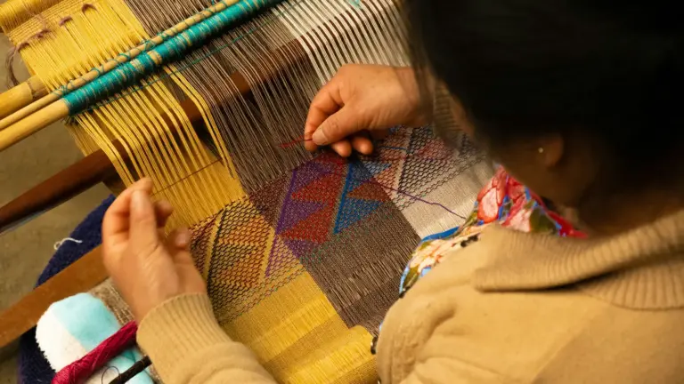 Hands working a wooden handloom weaving cotton cloth