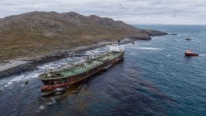 Grounded oil tanker leaking a dark sheen near a rocky Arabian Sea island