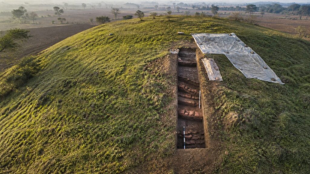 A protected archaeological mound near Ujjain with a carefully gridded excavation trench exposing ancient brick courses