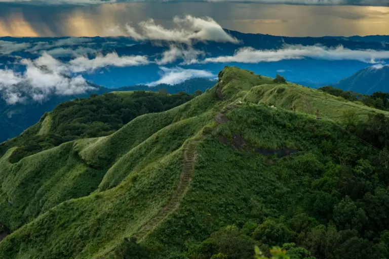 Green ridgelines and a hill trail at Reiek in Mizoram, under drifting rain clouds