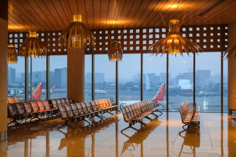 Rows of empty seats in a departure lounge at Mumbai airport, with Air India aircraft parked beyond the glass