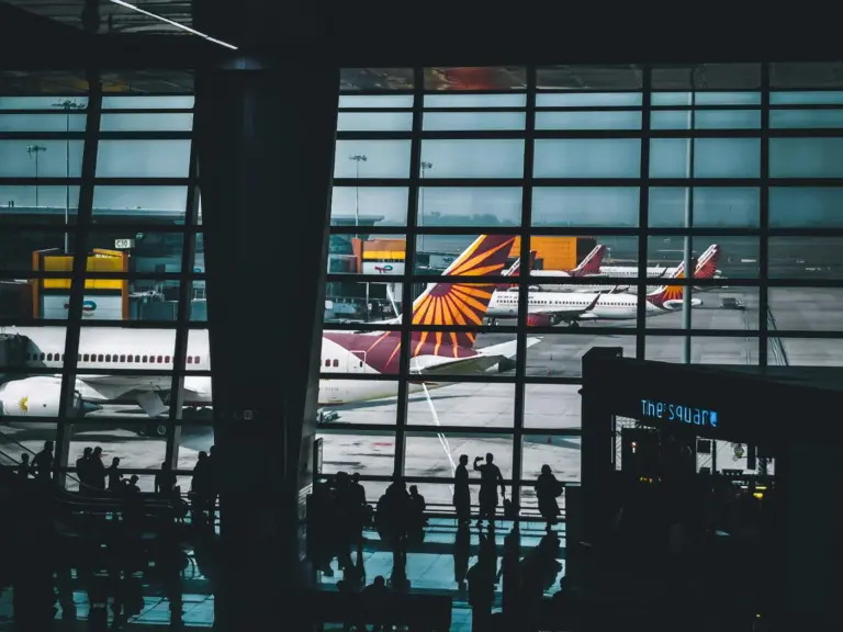 Silhouetted travellers inside a Delhi airport terminal, with Air India aircraft parked beyond the glass