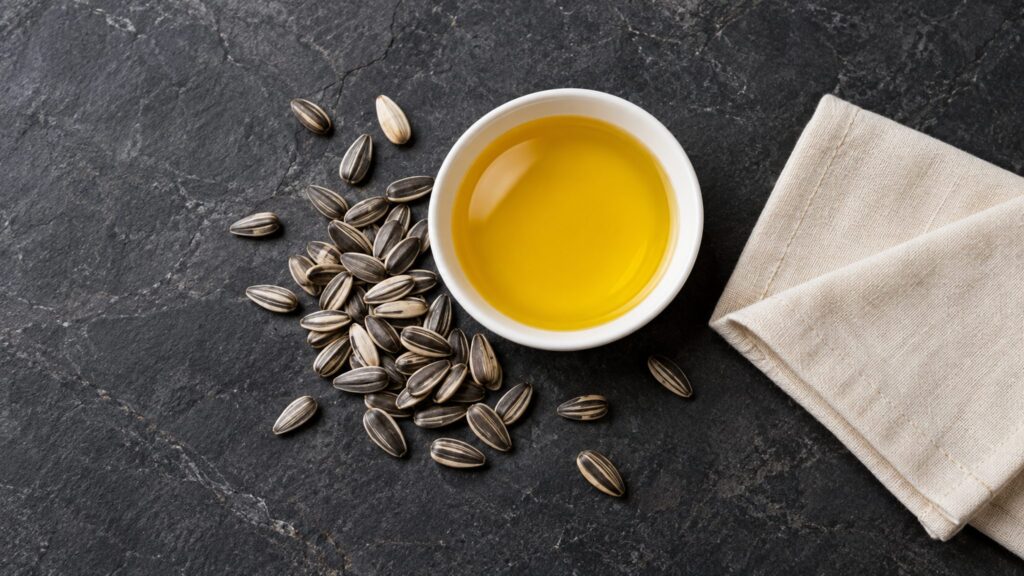 Illustrative bowl of sunflower oil beside sunflower seeds on dark stone