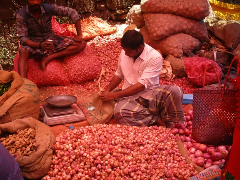 Vendors among heaps of small red onions, sacks and a weighing scale at a market in Kodaikanal, Tamil Nadu
