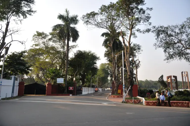 The main entrance gates of Fort William in Kolkata, set between red pillars and tall trees on a quiet road
