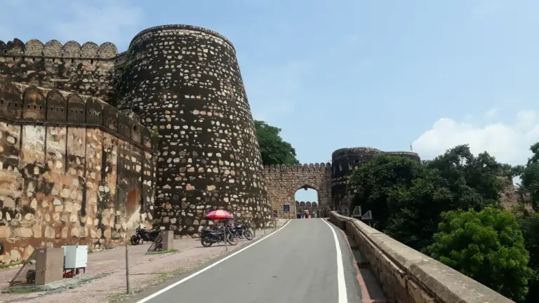 Massive round stone bastions and crenellated walls of Jhansi Fort, with a road leading up to an arched gateway