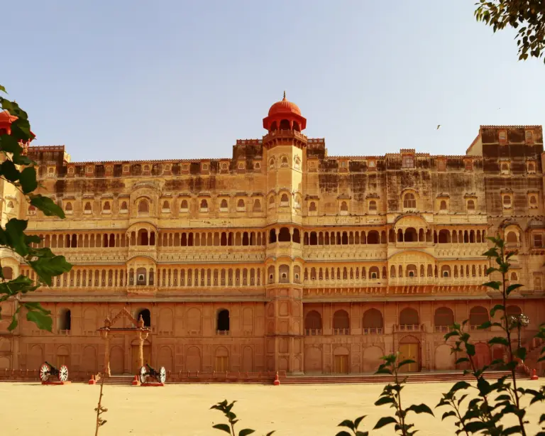 Sandstone facade of Junagarh Fort in Bikaner, with tiers of balconied windows, a red-domed tower and cannons in front