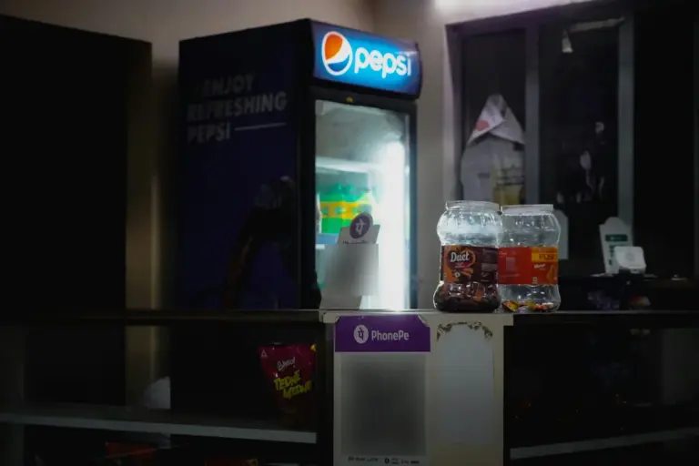 A PhonePe UPI QR code standee on a small shop counter in front of a lit drinks cooler