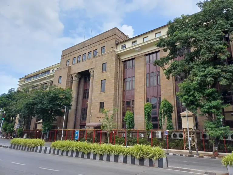 The columned stone facade of the Reserve Bank of India building on a tree-lined street in Mumbai