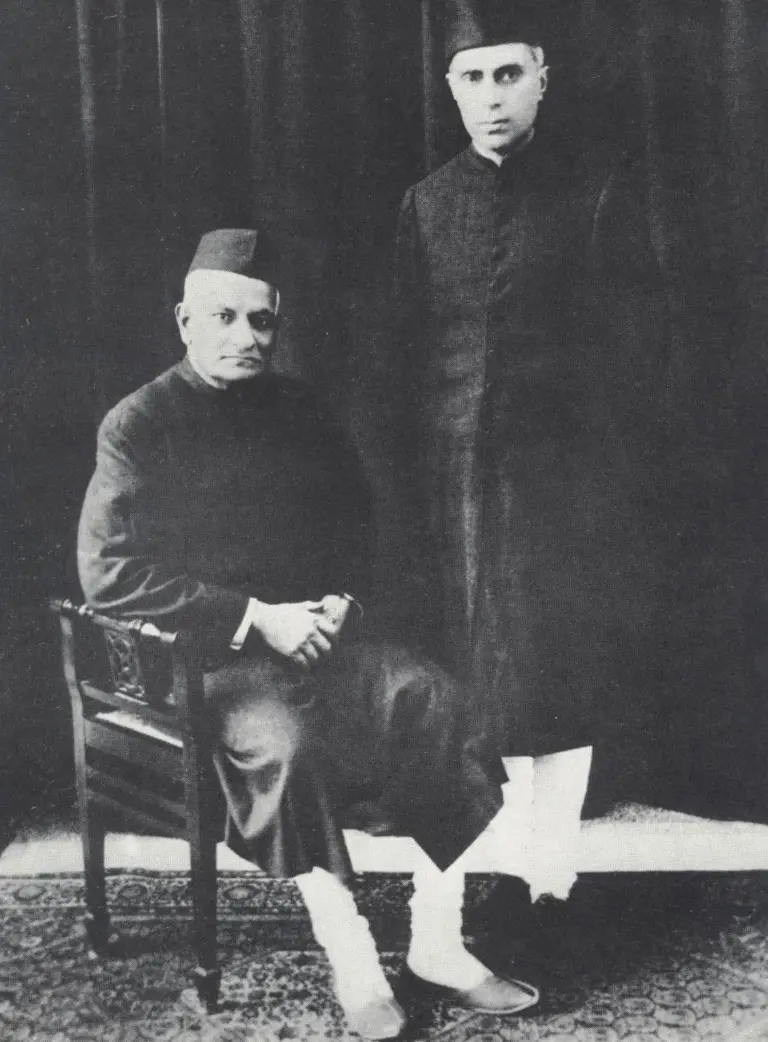 Motilal Nehru seated beside his son Jawaharlal Nehru, standing, both in dark sherwanis and caps, in a 1929 studio portrait