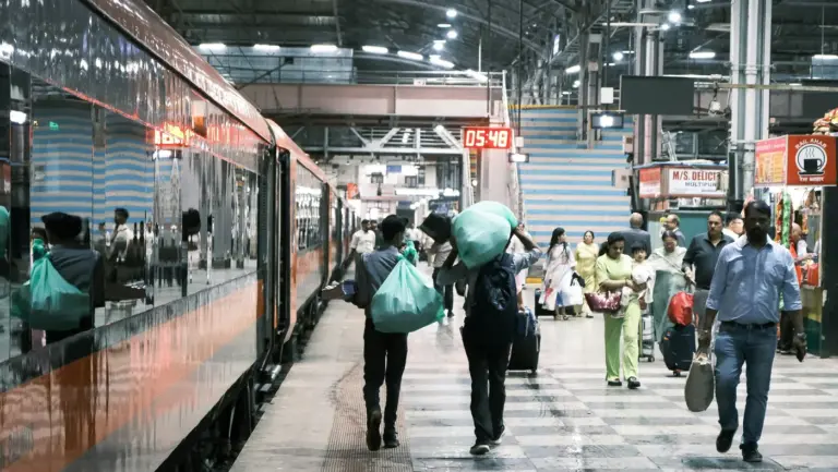 Passengers carrying luggage along a platform beside a train at Mumbai Central railway station