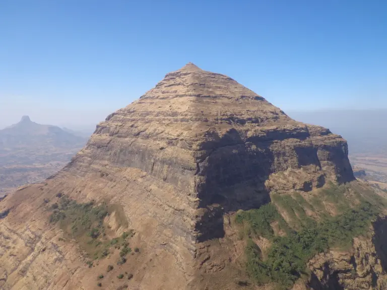 The steep, layered basalt peak of Salher fort in Nashik district, Maharashtra, under a clear blue sky