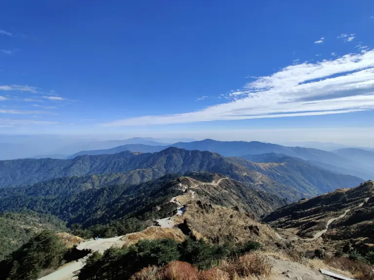 A dirt track winding along the forested Singalila ridge near Phalut, West Bengal, above layers of blue hills