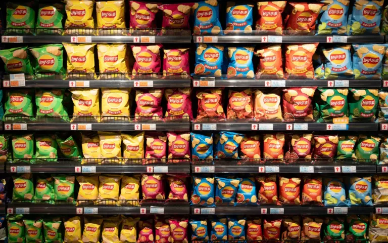 Rows of colorful potato chip packets stacked tightly on supermarket shelves, filling the frame from top to bottom.