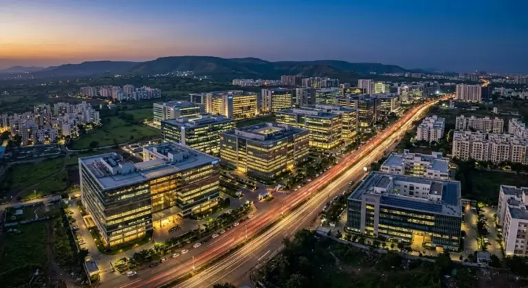 Aerial dusk view of lit glass office blocks in the Hinjewadi IT park, Pune, beside a highway streaked with light trails