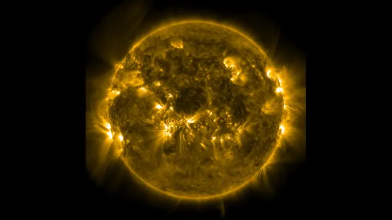 The Sun seen in extreme ultraviolet light, glowing gold with bright active regions and looping plasma along its edge on a black background.