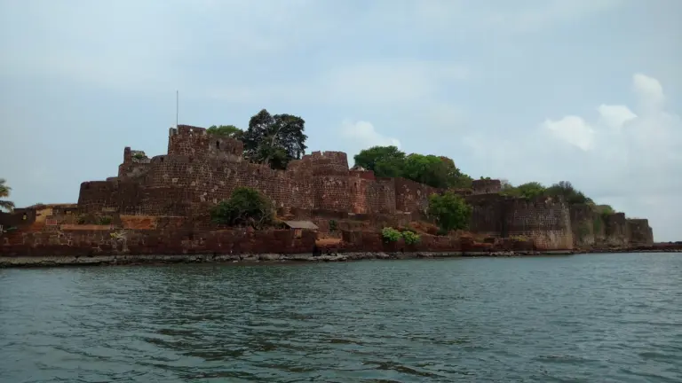 Laterite walls and bastions of Vijaydurg sea fort rising from the water's edge, seen from a boat