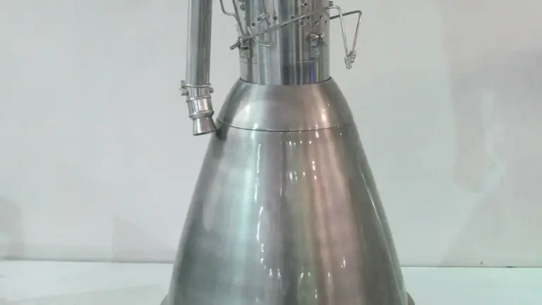 A polished metal scale model of the Vikas rocket engine, with a flared nozzle bell and pipework, stands against a plain white wall.