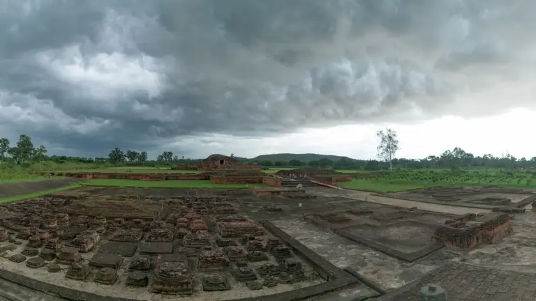 Excavated brick ruins of the Vikramashila Mahavihara at Antichak, Bihar, with rows of votive stupa bases under a stormy sky