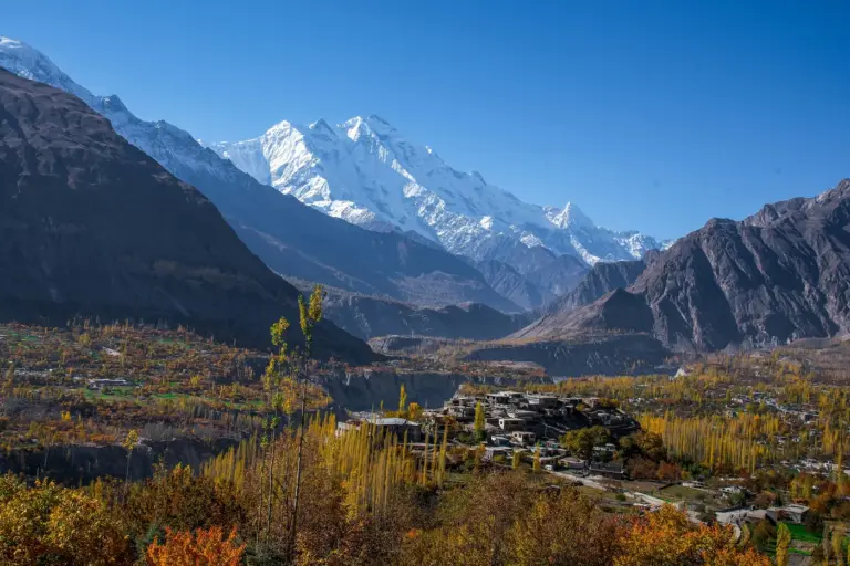 Snow-covered Rakaposhi peak rising above autumn poplars and village houses in the Hunza valley.