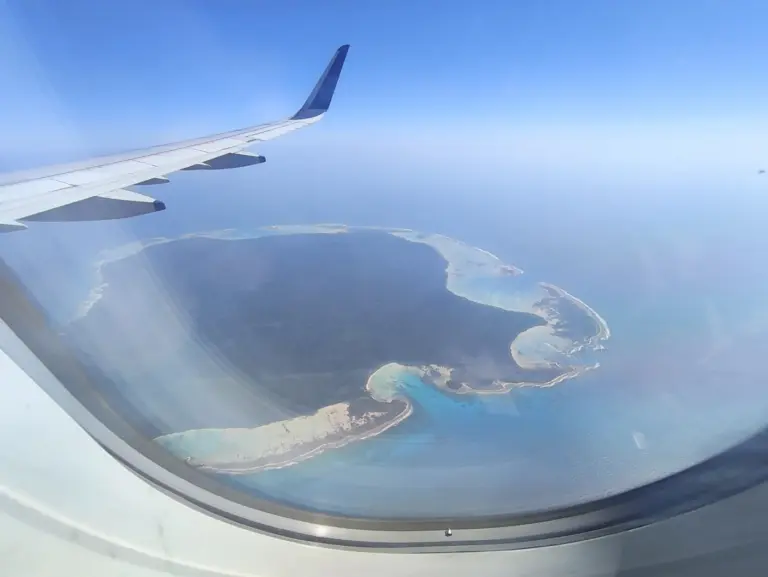 Aerial view from an aircraft window of North Sentinel Island, a forested island ringed by pale coral reef.
