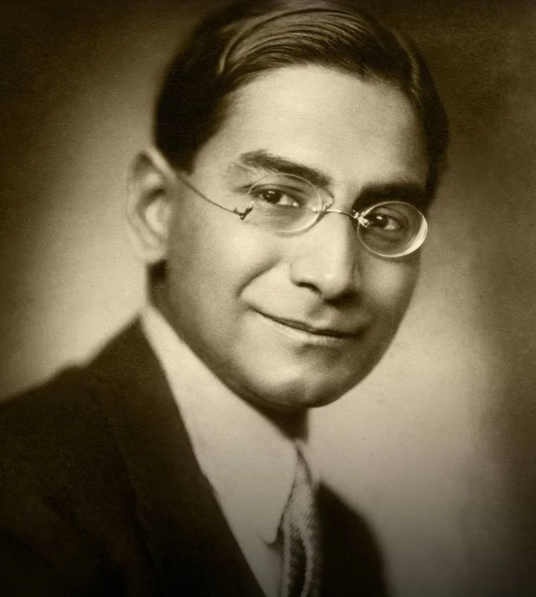 A sepia studio portrait of a young Prasanta Chandra Mahalanobis wearing round spectacles and a suit.