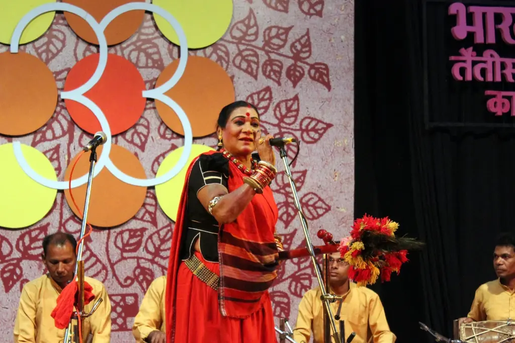 Teejan Bai performing Pandavani on stage at Bharat Bhavan, Bhopal, holding her decorated tambura, with accompanists seated behind her.